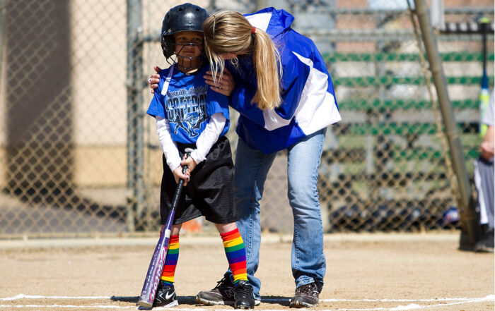 A coach helps a young softball player in colorful socks at a camp.