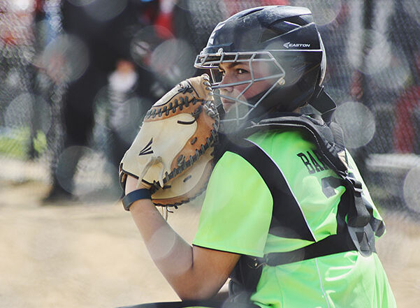 Youth softball catcher in gear, holding a glove, at a camp.