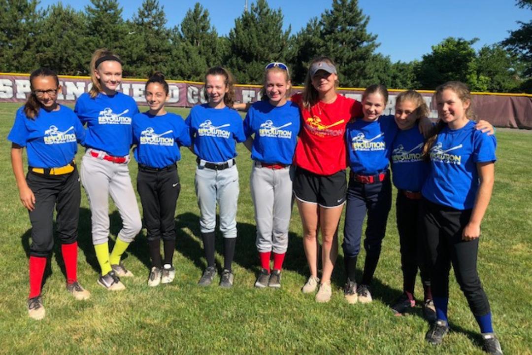 A group of young softball players and a coach smiling on a field.