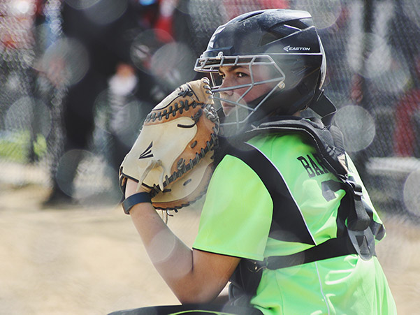 A softball catcher crouches in position and prepares herself for the next play.